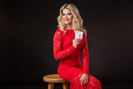 Young woman in red dress in casino with cards over black background. Poker