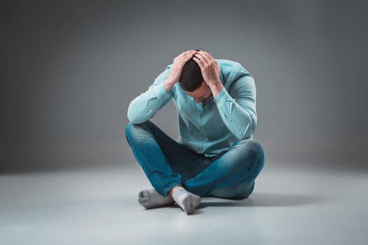 Young depressed man sitting holding his head with both hands. Studio shot.