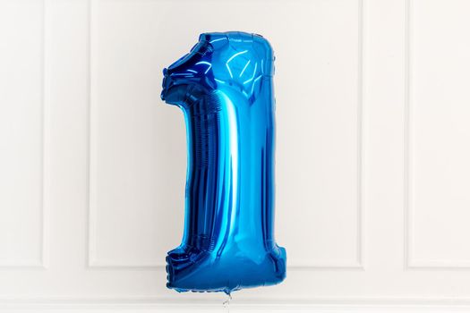 Birthday blue air balloon in shape of number one with white wall on background at home