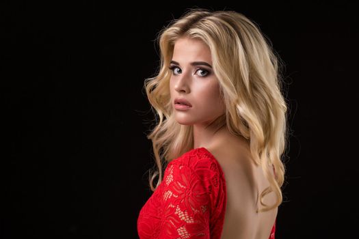 Beautiful sexy blonde woman in a red dress on black background, party.