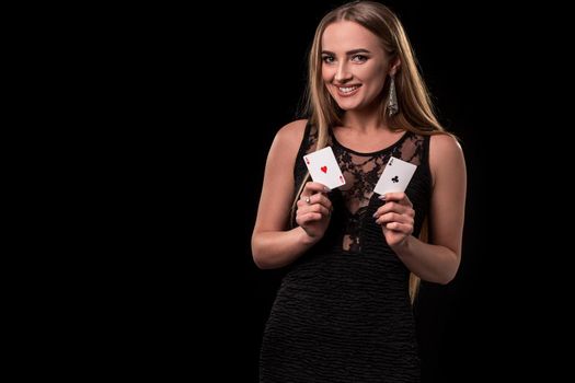 Young beautiful woman in a sexy black dress playing in casino. Girl holding the winning combination of poker cards on a black background. Two aces