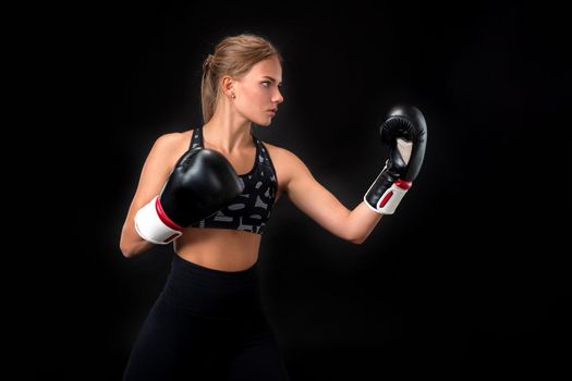 Beautiful female athlete in boxing gloves, in the studio on a black background. The boxer fulfills the blow