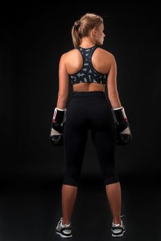 Young woman wearing boxer gloves back view at the studio on a black background.