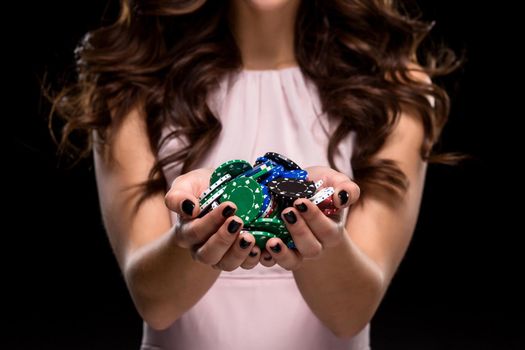 Sexy woman in a chic gently pink dress holding colored poker chips on a black background. Woman winning. Casino. Poker. Victory. Luck. Close-up of poker chips