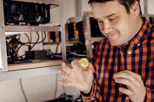 A man eagerly holds a gold coin against the background of computer equipment. Man love money