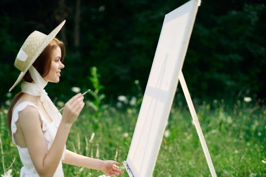 Woman in white dress in nature paints a picture of a landscape hobby. High quality photo