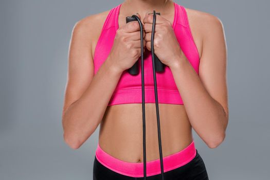 Full length image of a pretty fitness woman doing exercise with skipping rope over gray background. Young woman with beautiful slim healthy body posing in studio. Close-up