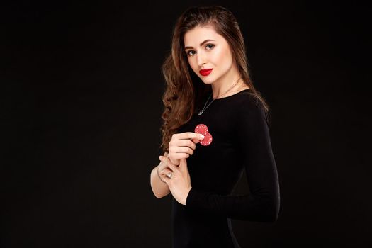 Sexy curly hair brunette in black dress posing with chips in her hands, poker concept black background. Casino, poker, Roulette Blackjack Spin.