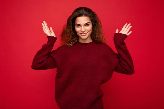 Young beautiful curly brunette woman with sincere emotions poising isolated on background wall with copy space wearing casual dark red sweater. Happy concept.