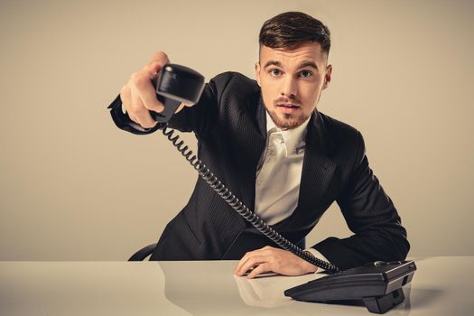 Portrait of attractive businessman holding telephone in his hand. This call is for you concept. A young man in a black suit dials the phone number while sitting in the office