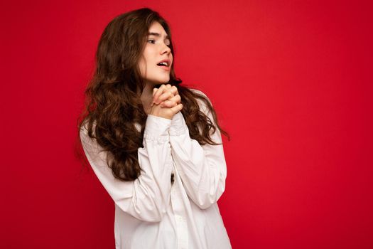 Portrait of nice cute young curly brunet female person wearing white shirt isolated on red background with free space, wanting and dreaming with sincere emotions.