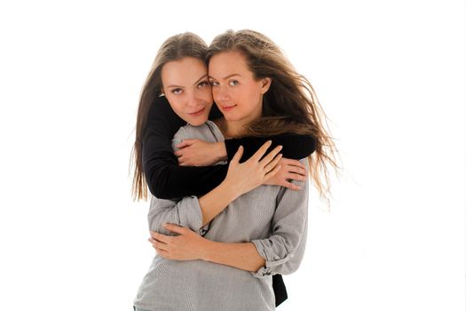 Charming brown haired woman looking at camera while hugging from behind female friend in casual wear isolated on white background