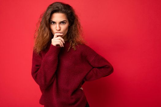 Young beautiful thoughtful serious curly brunette woman with sincere emotions poising isolated on background wall with copy space wearing casual dark red sweater. Think concept.
