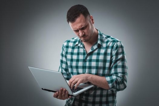 Attractive business man model in green shirt isolated on gray working with laptop, showing something by left hand. Caucasian guy.