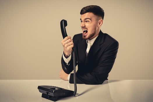 A young man in a black suit dials the phone number while sitting in the office. Manager talking on the phone. Man emotionally shouts