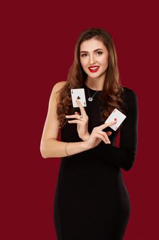 Beautiful caucasian woman in black dress with poker cards gambling in casino. Studio shot on red background. Poker. Two Aces in Hand