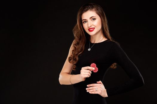 Sexy curly hair brunette in black dress posing with chips in her hands, poker concept black background. Casino, poker, Roulette Blackjack Spin.