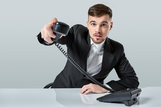 Portrait of attractive businessman holding telephone in his hand. This call is for you concept. A young man in a black suit dials the phone number while sitting in the office