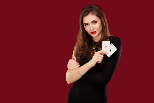 Beautiful caucasian woman in black dress with poker cards gambling in casino. Studio shot on red background. Poker. Two Aces in Hand