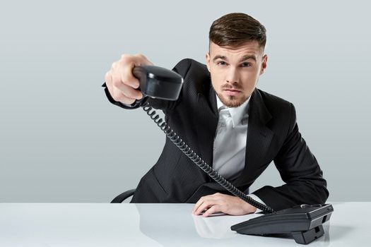 Portrait of attractive businessman holding telephone in his hand. This call is for you concept. A young man in a black suit dials the phone number while sitting in the office