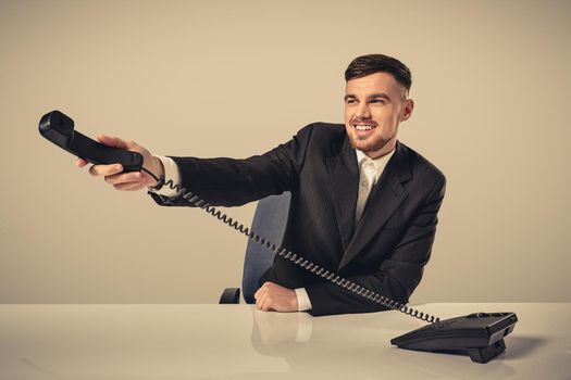 Portrait of attractive businessman holding telephone in his hand. This call is for you concept. A young man in a black suit dials the phone number while sitting in the office