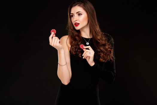 Sexy curly hair brunette in black dress posing with chips in her hands, poker concept black background. Casino, poker, Roulette Blackjack Spin.