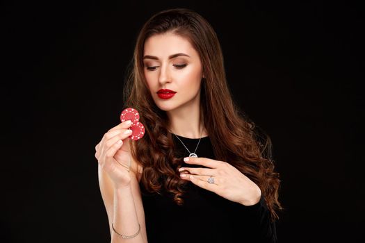 Sexy curly hair brunette in black dress posing with chips in her hands, poker concept black background. Casino, poker, Roulette Blackjack Spin.