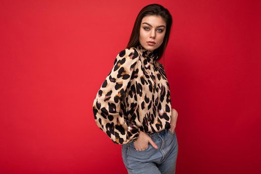 Image of a beautiful young brunette woman dressed in animal printed blouse posing isolated over red background with copy space.