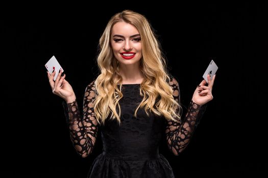 Beautiful young woman in black dress holding two ace of cards in her hand, isolated on black background. Poker. Casino. Roulette Blackjack Spin. Caucasian woman looking at camera