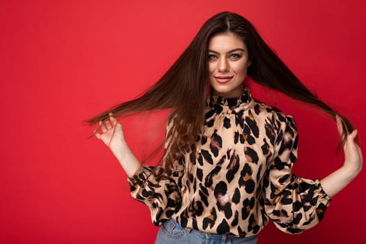 Fashion photo of young beautiful fashionable sexy brunette woman wearing stylish leopard blouse isolated on red background with empty space.