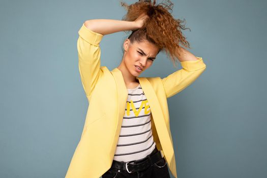 Young crazy funny beautiful curly brunette woman with sincere emotions poising isolated over background wall with empty space wearing casual yellow jacket. Emotional concept.