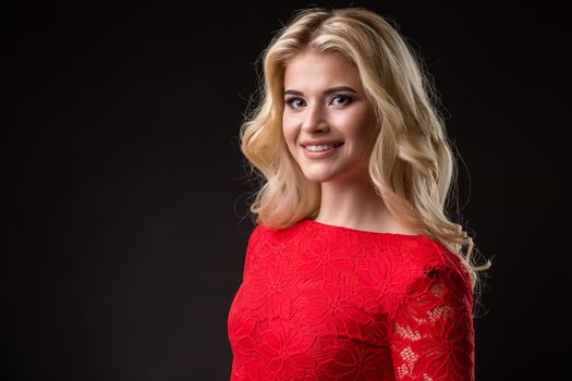 Beautiful woman with long blond hair. Fashion model posing at studio. Young woman in a red dress