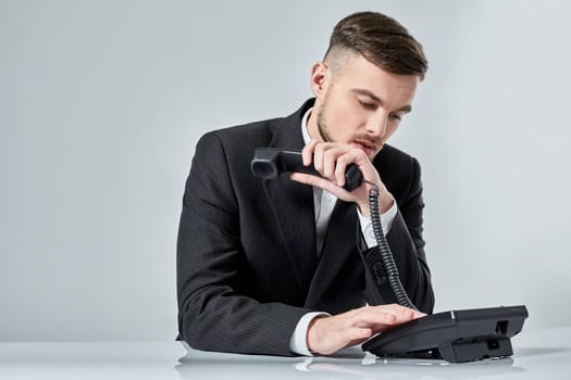 A young man dressed in a black suit dials the phone number while sitting in the office