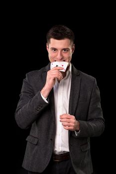 Young caucasian man in a dark suit and a white shirt holding two aces in his hand and teeth on black background. Gambling concept. Casino