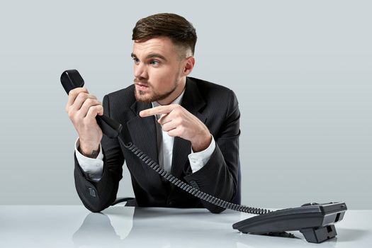 Portrait of attractive businessman holding telephone in his hand. This call is for you concept. A young man in a black suit dials the phone number while sitting in the office