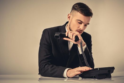 A young man dressed in a black suit dials the phone number while sitting in the office