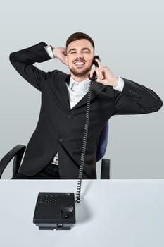 A young man in a black suit dials the phone number while sitting in the office. Manager talking on the phone