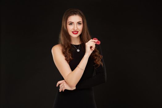 Sexy curly hair brunette in black dress posing with chips in her hands, poker concept black background. Casino, poker, Roulette Blackjack Spin.