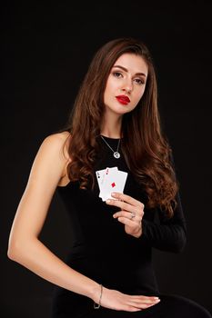 Attractive young woman in a sexy black dress holding the winning combination of poker cards. Two Aces. Studio shot on a black background. Casino