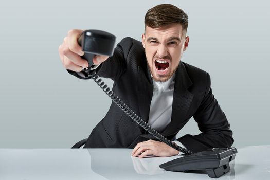 A young man in a black suit dials the phone number while sitting in the office. Manager talking on the phone. Man emotionally shouts