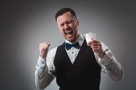 Handsome confident man holding cards looking at camera. Studio shot on gray background. Two Aces. Emotions happy win