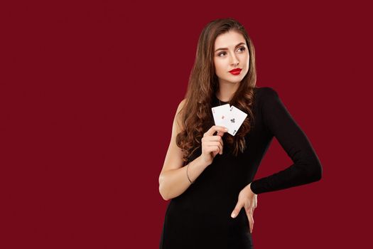 Beautiful caucasian woman in black dress with poker cards gambling in casino. Studio shot on red background. Poker. Two Aces in Hand