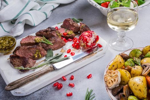 Kangaroo meat steak with green pesto and pomegranate on white wooden cutting board. Helthy holiday food concept. Selective focus.