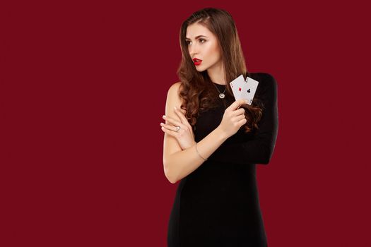 Beautiful caucasian woman in black dress with poker cards gambling in casino. Studio shot on red background. Poker. Two Aces in Hand