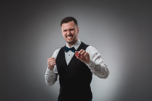 Young man in shirt and waistcoat shows his poker chips, studio shot. Poker. Emotions