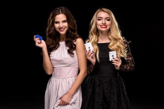 Two Sexy girls brunette and blonde, posing with chips and two cards aces in her hands, poker concept black background. Casino, poker, Roulette Blackjack Spin. big win
