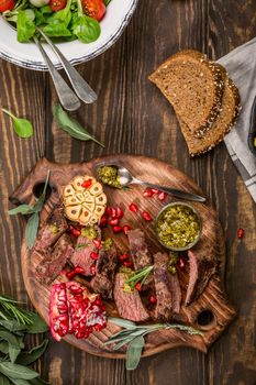 Kangaroo meat steak with green pesto and pomegranate on wooden cutting board. Helthy holiday food concept. Top view.