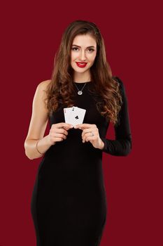 Beautiful caucasian woman in black dress with poker cards gambling in casino. Studio shot on red background. Poker. Two Aces in Hand