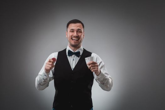 Young man in shirt and waistcoat shows his cards and holds poker chips in his hands, studio shot. Poker. Emotions