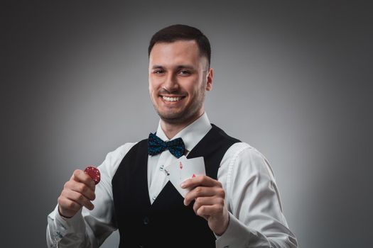 Young man in shirt and waistcoat shows his cards and holds poker chips in his hands, studio shot. Poker. Emotions
